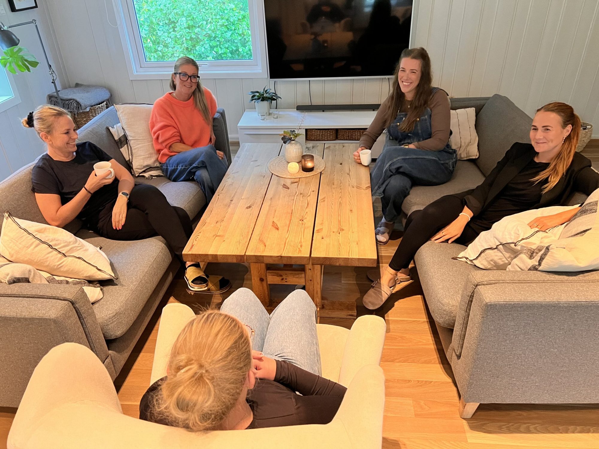Fem damer sitter i sofaer rundt et bord